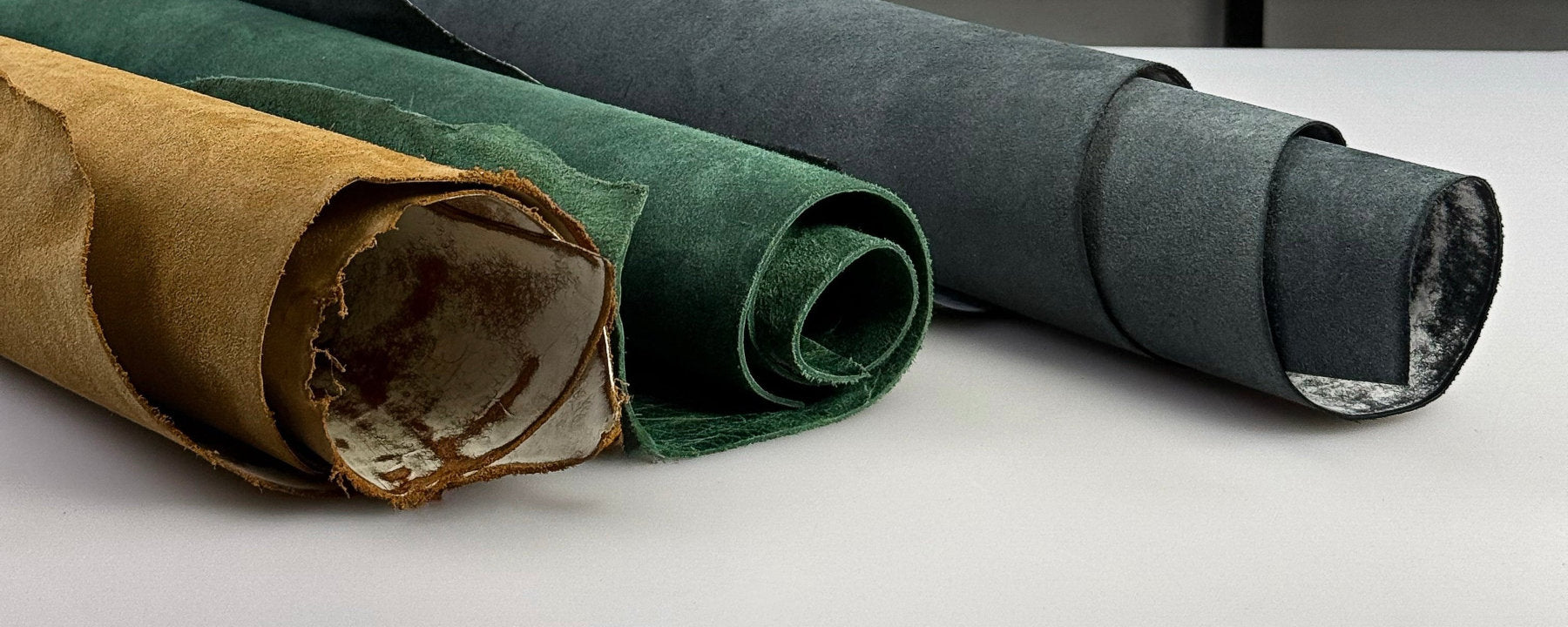 Three rolled pieces of premium Italian leather in warm tones Winds Leather branding