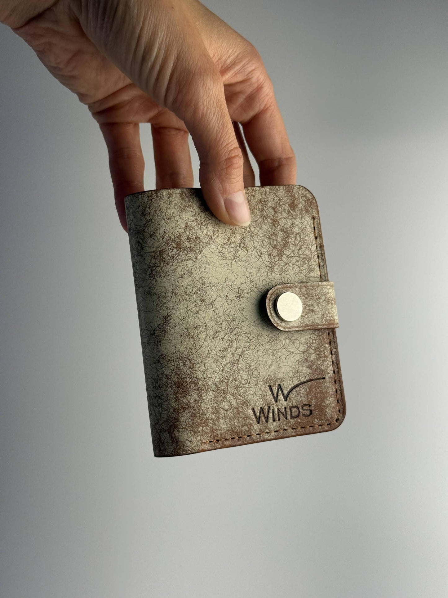 brown glance leather wallet with button closure, front side view with hand and Winds logo, on white background