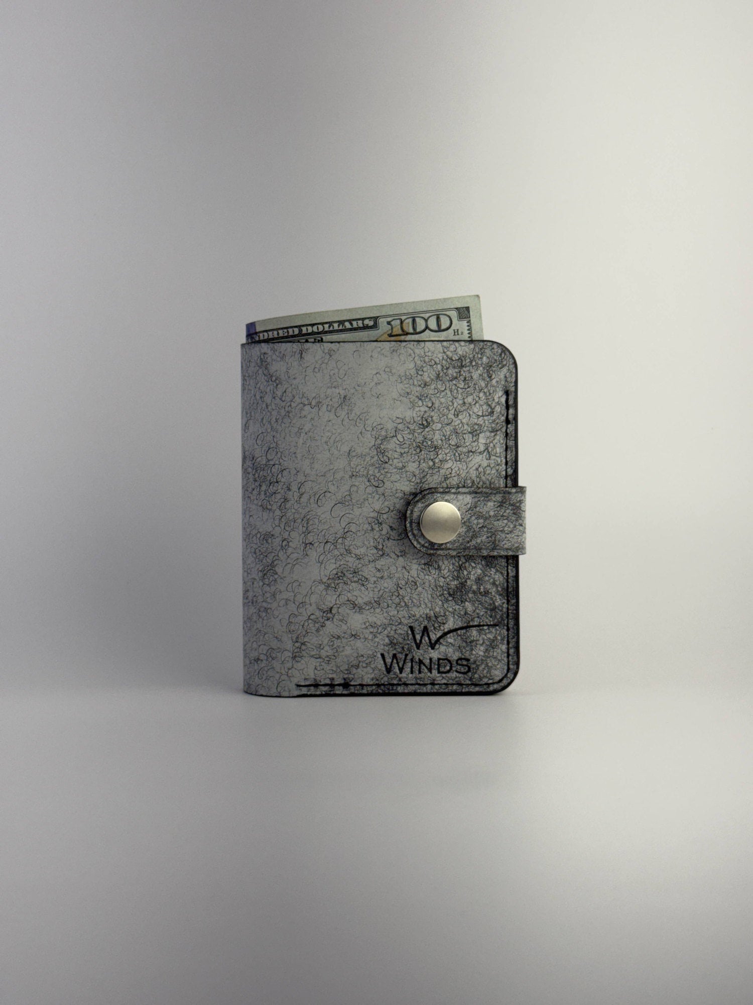 black glance leather wallet with button closure closed front view with cash and Winds logo on white background
