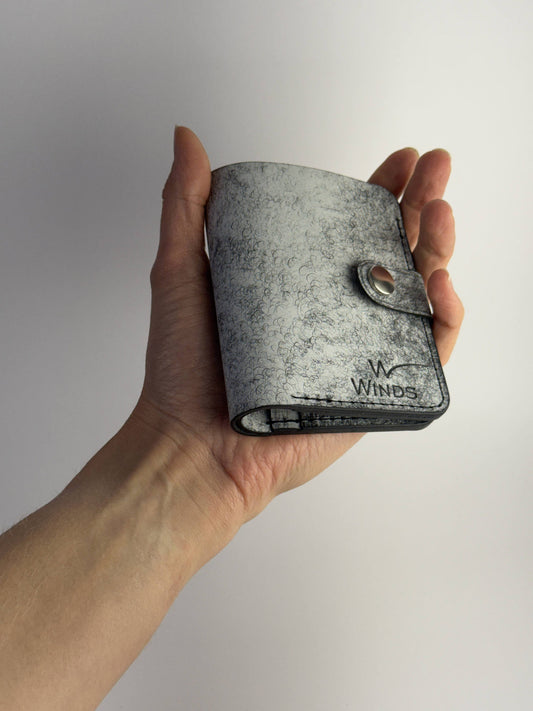 black glance leather wallet with button closure, front view with hand and Winds logo, on a white background