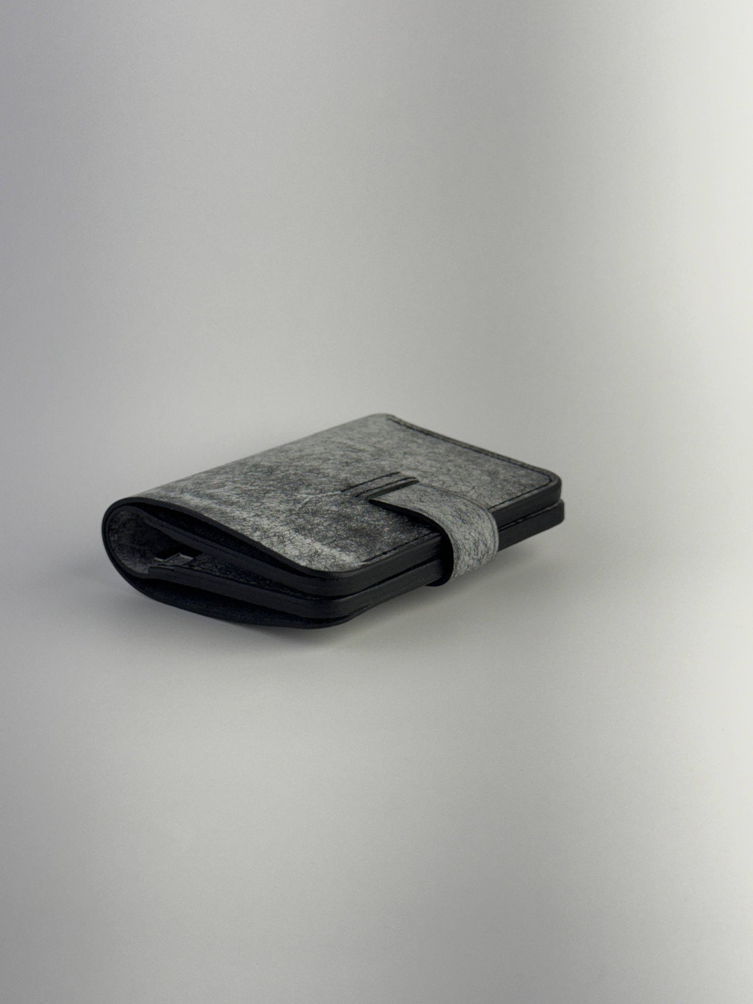 black glance leather wallet with button closure lying closed back side view on white background