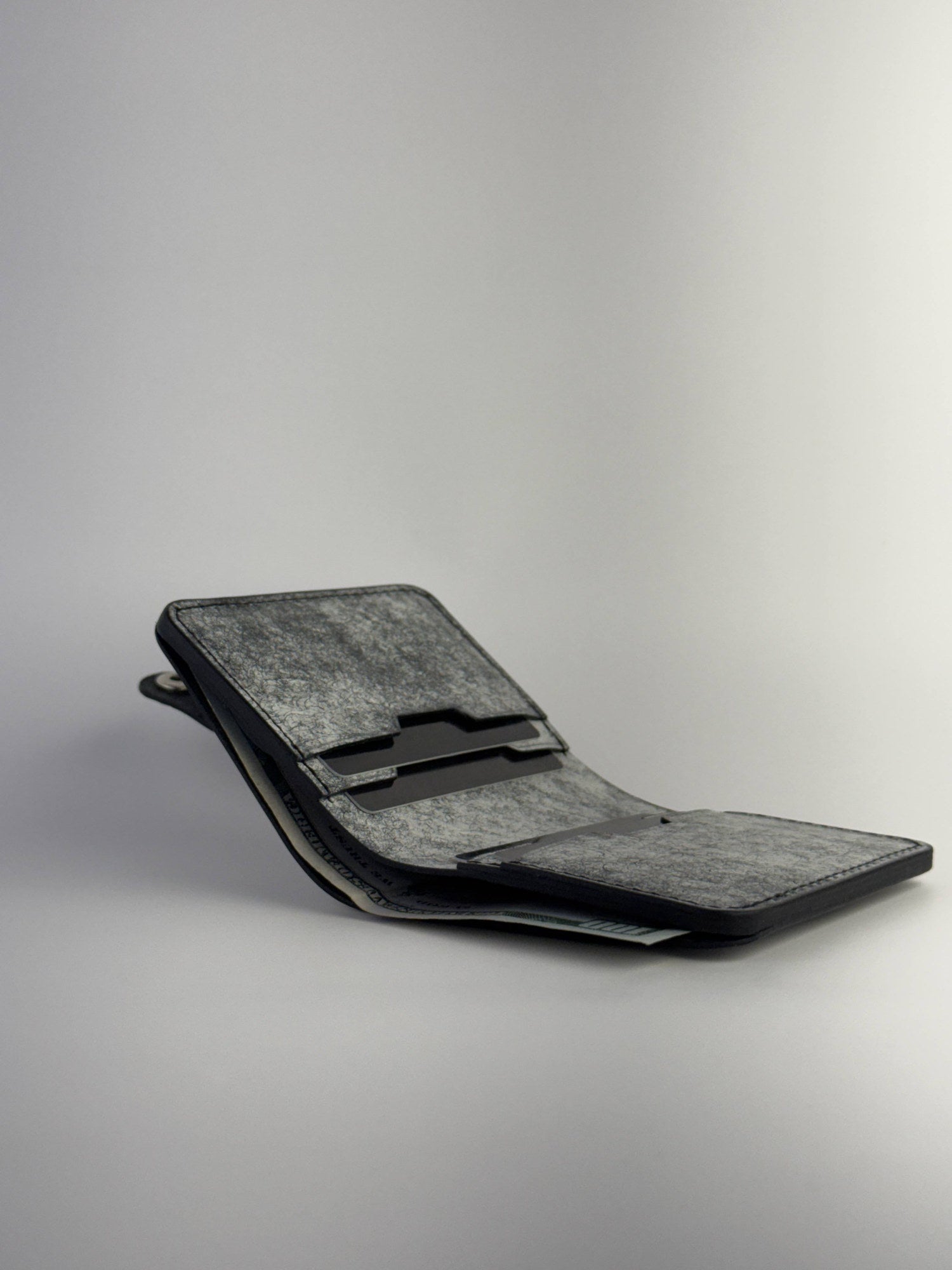 black glance leather wallet with button closure lying opened with cards and cash side view on white background