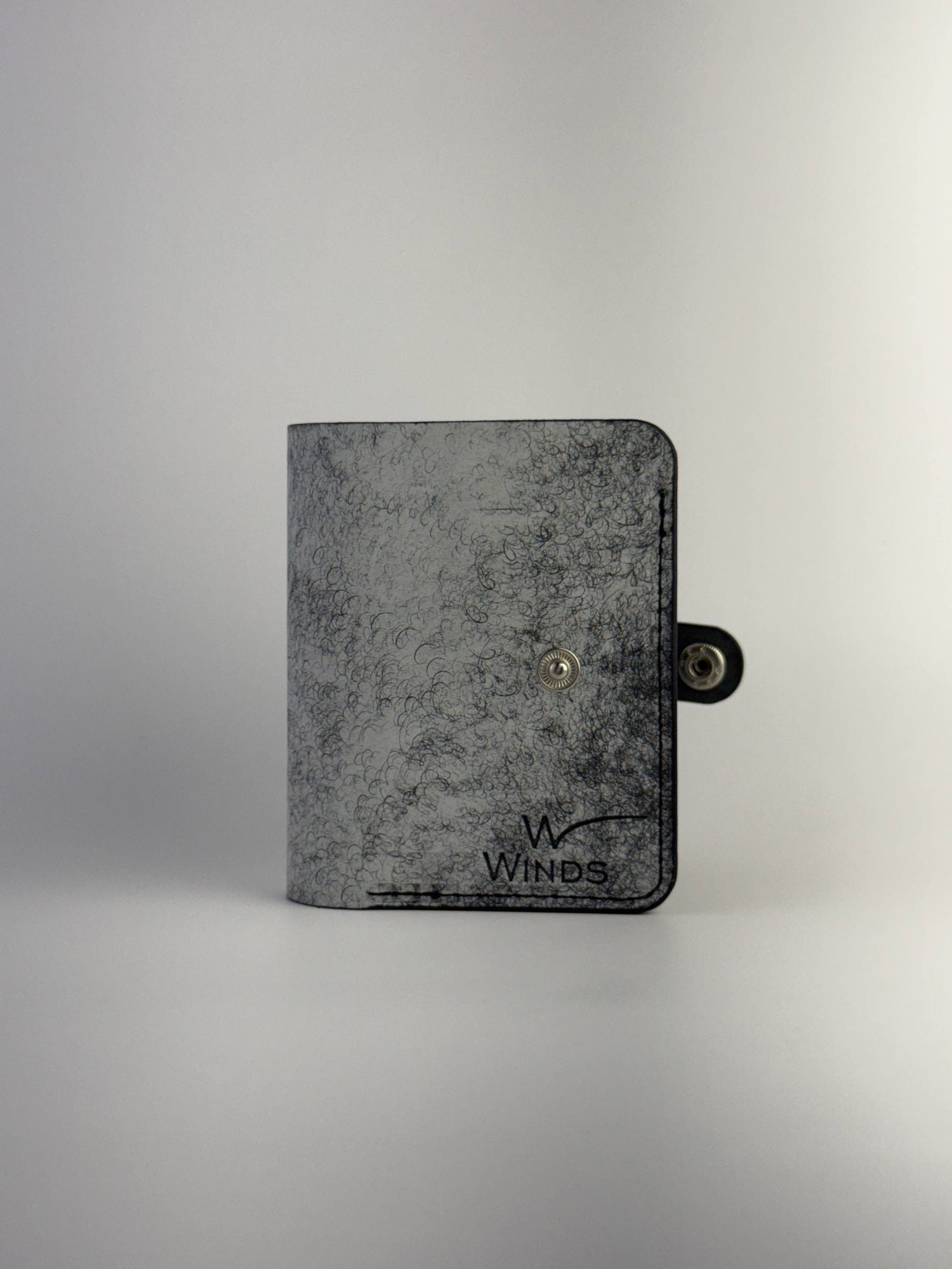 black glance leather wallet with button closure opened front side view with Winds logo on white background